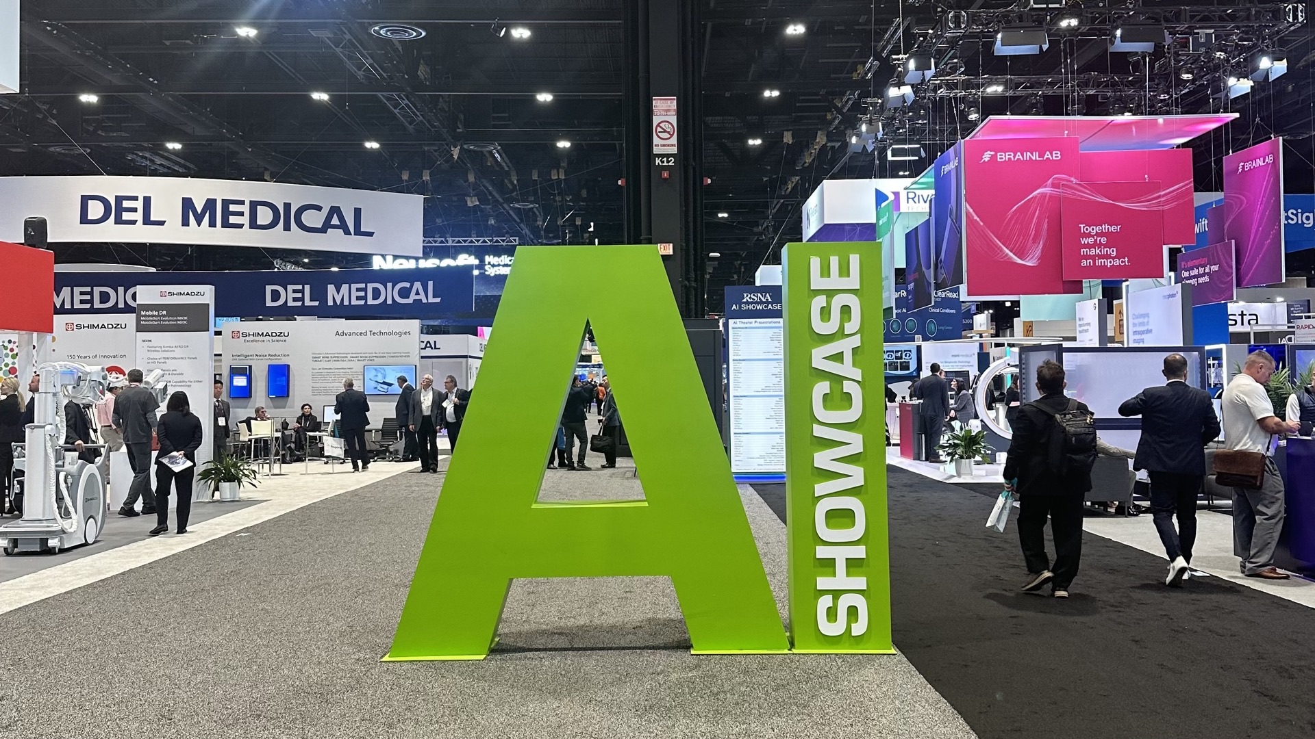A towering green 'AI Showcase' sign on a busy medical technology exhibition floor, surrounded by vendor booths and attendees walking the aisles